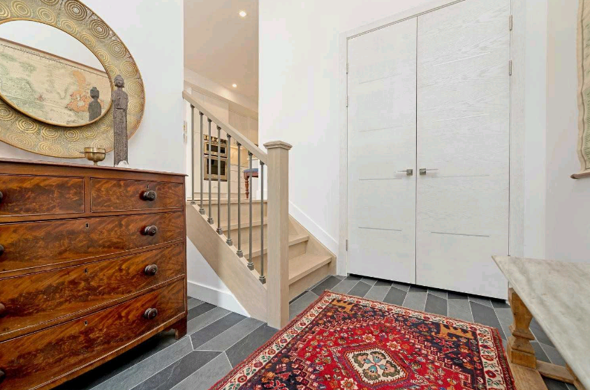 A hallway with stairs , a dresser , a rug and a mirror.