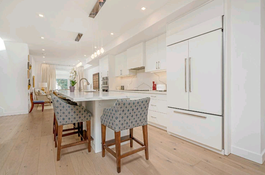 A kitchen with white cabinets , stools , a refrigerator and a large island.