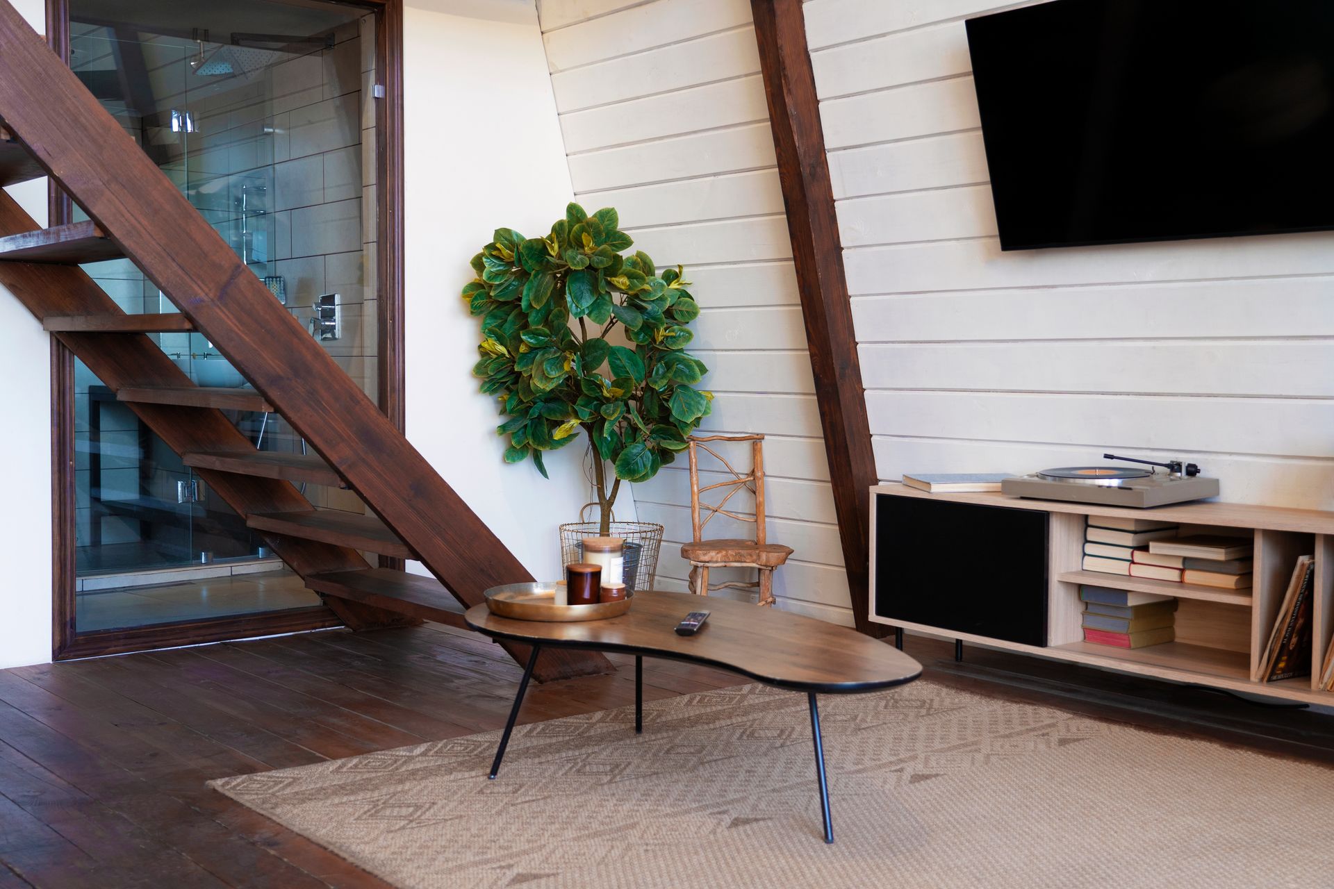 A living room with a wooden staircase , a coffee table and a flat screen tv.