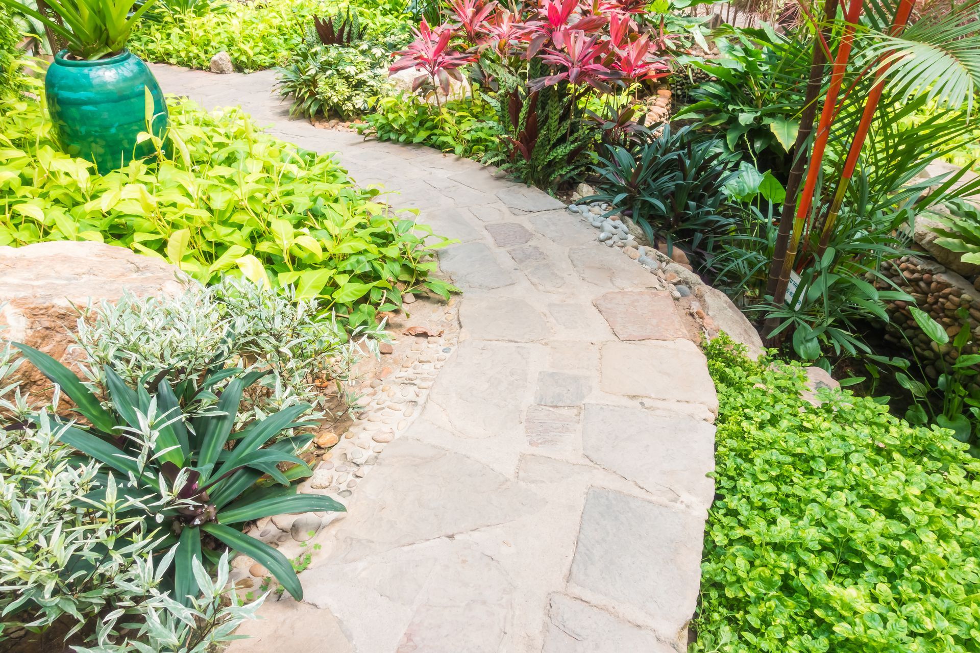 A stone walkway in a garden surrounded by lots of plants and flowers.