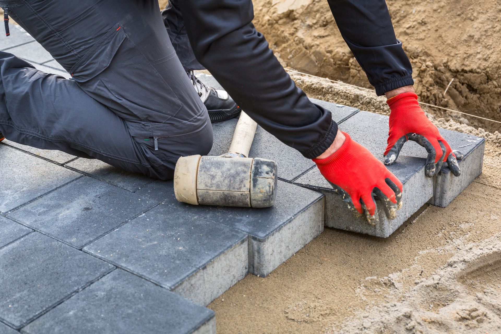 A person wearing red gloves is laying bricks on a sidewalk.