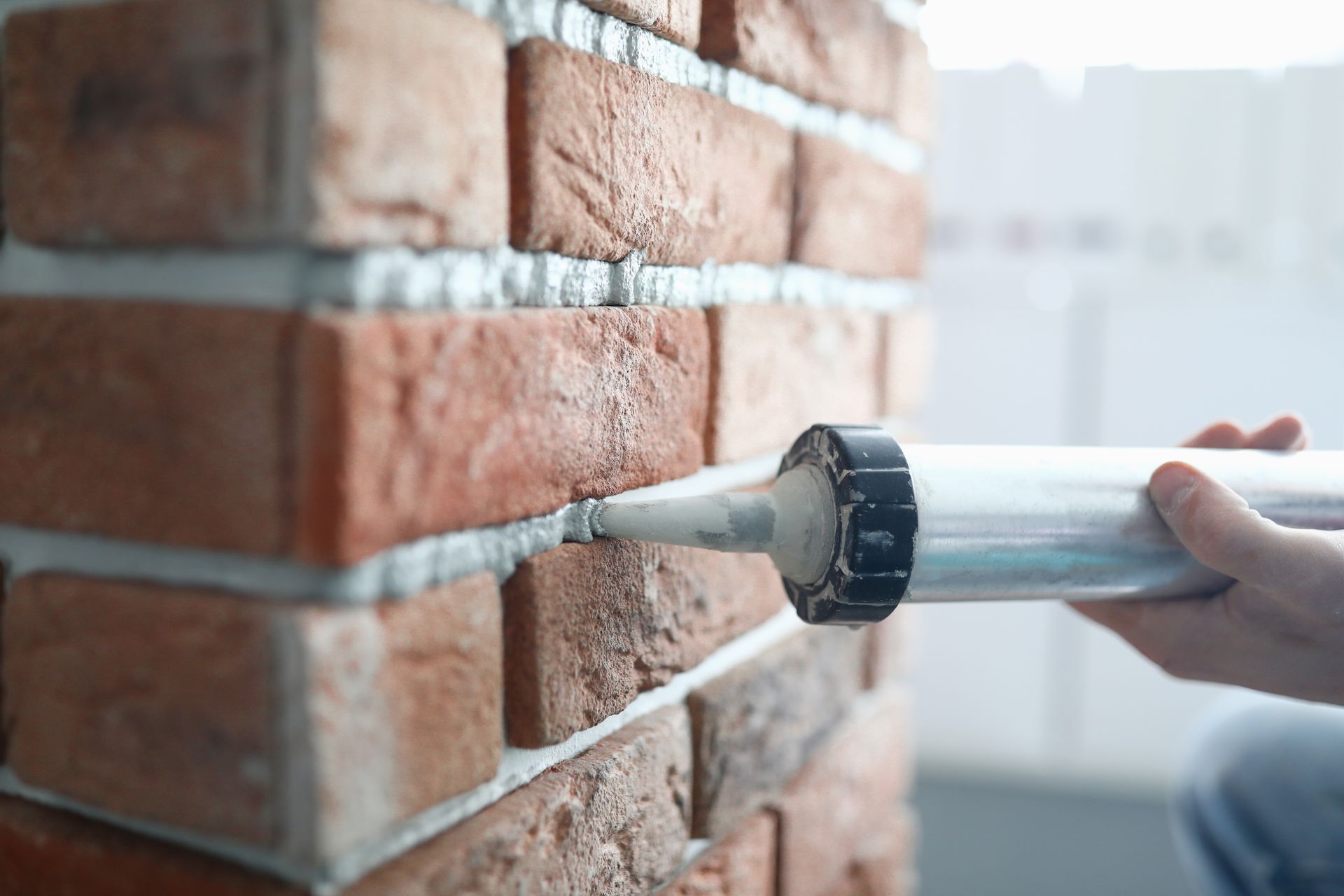 Caulking gun applying sealant to a brick wall seam