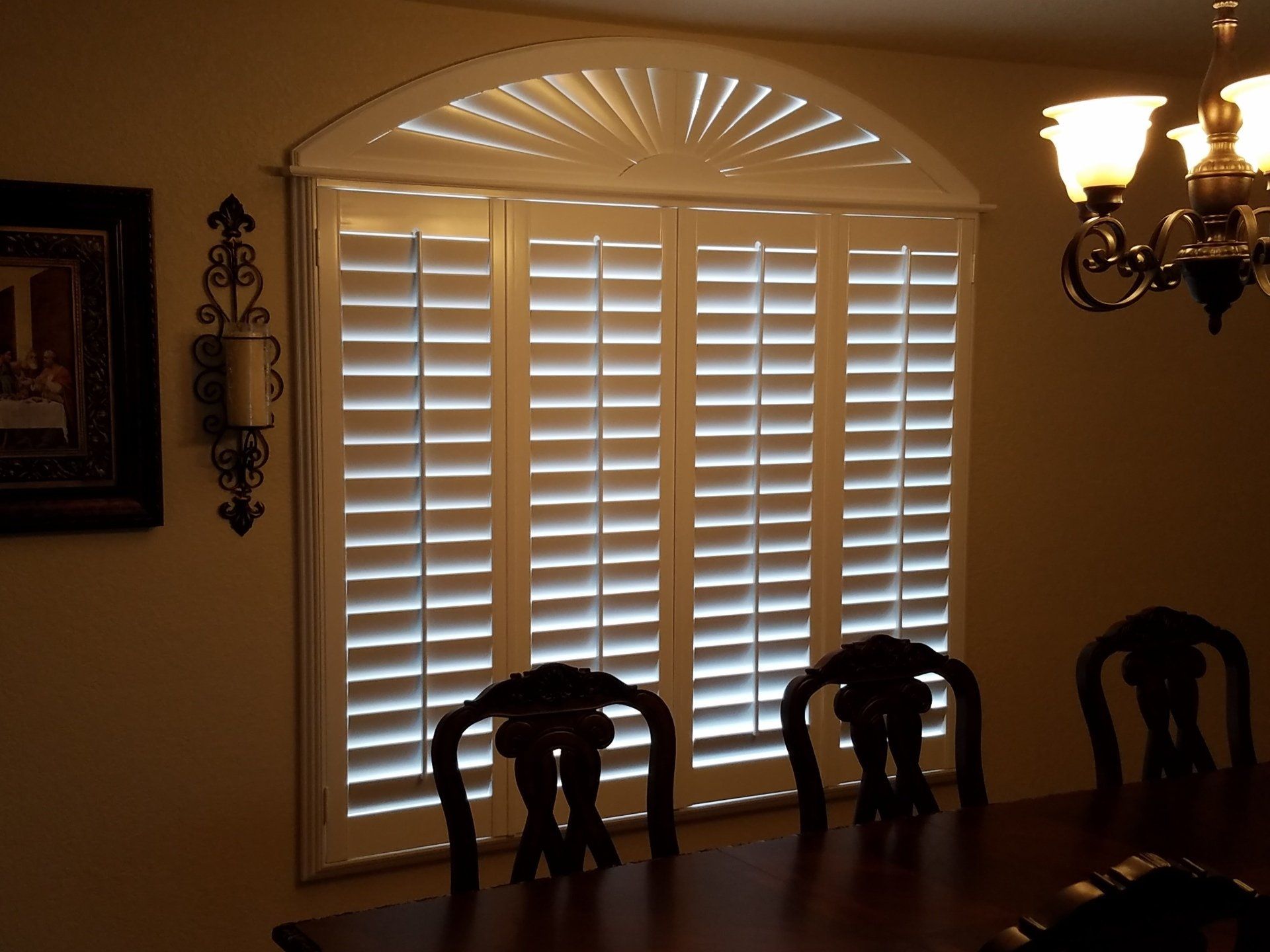A dining room with arched shutters and a chandelier