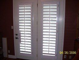 A pair of white shutters on a door in a room.