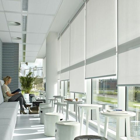 A woman sits on a couch reading a book in a room with tables and chairs