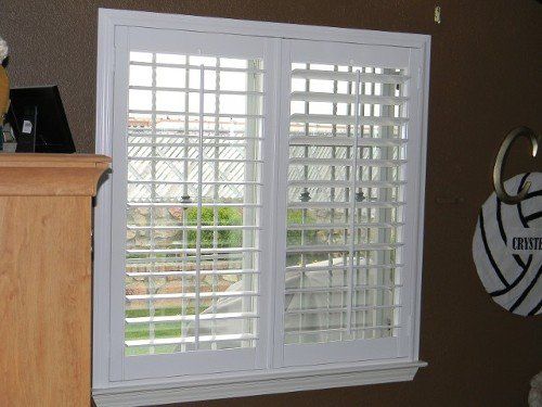 A window with white shutters and a volleyball hanging on the wall