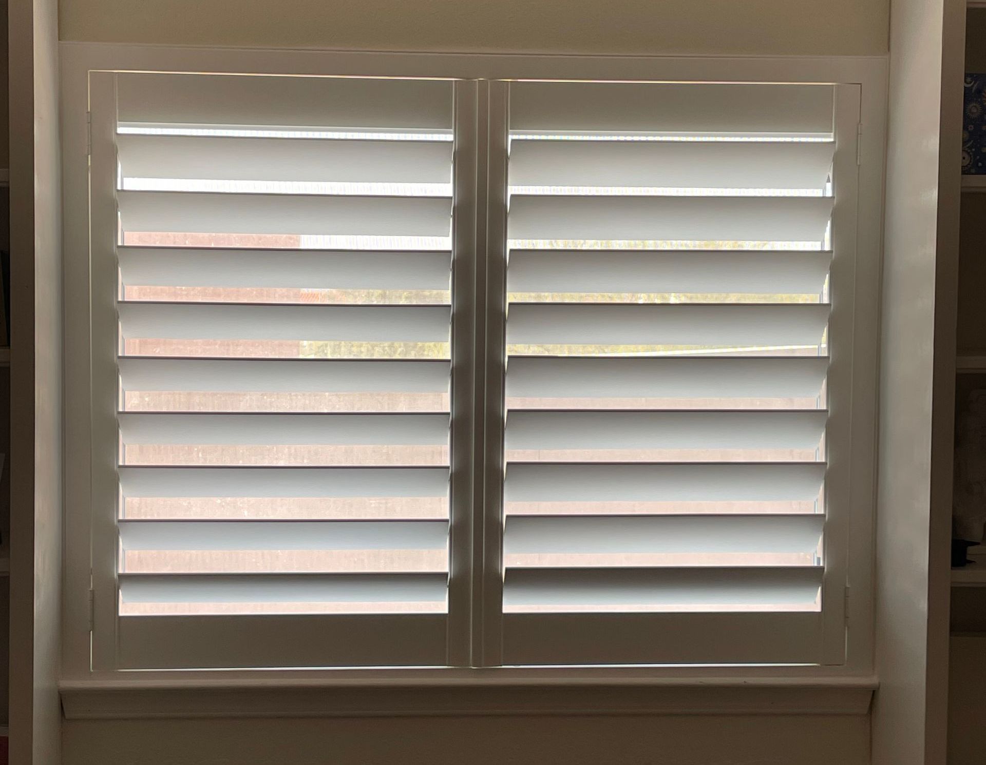 A window with white shutters on it in a room.