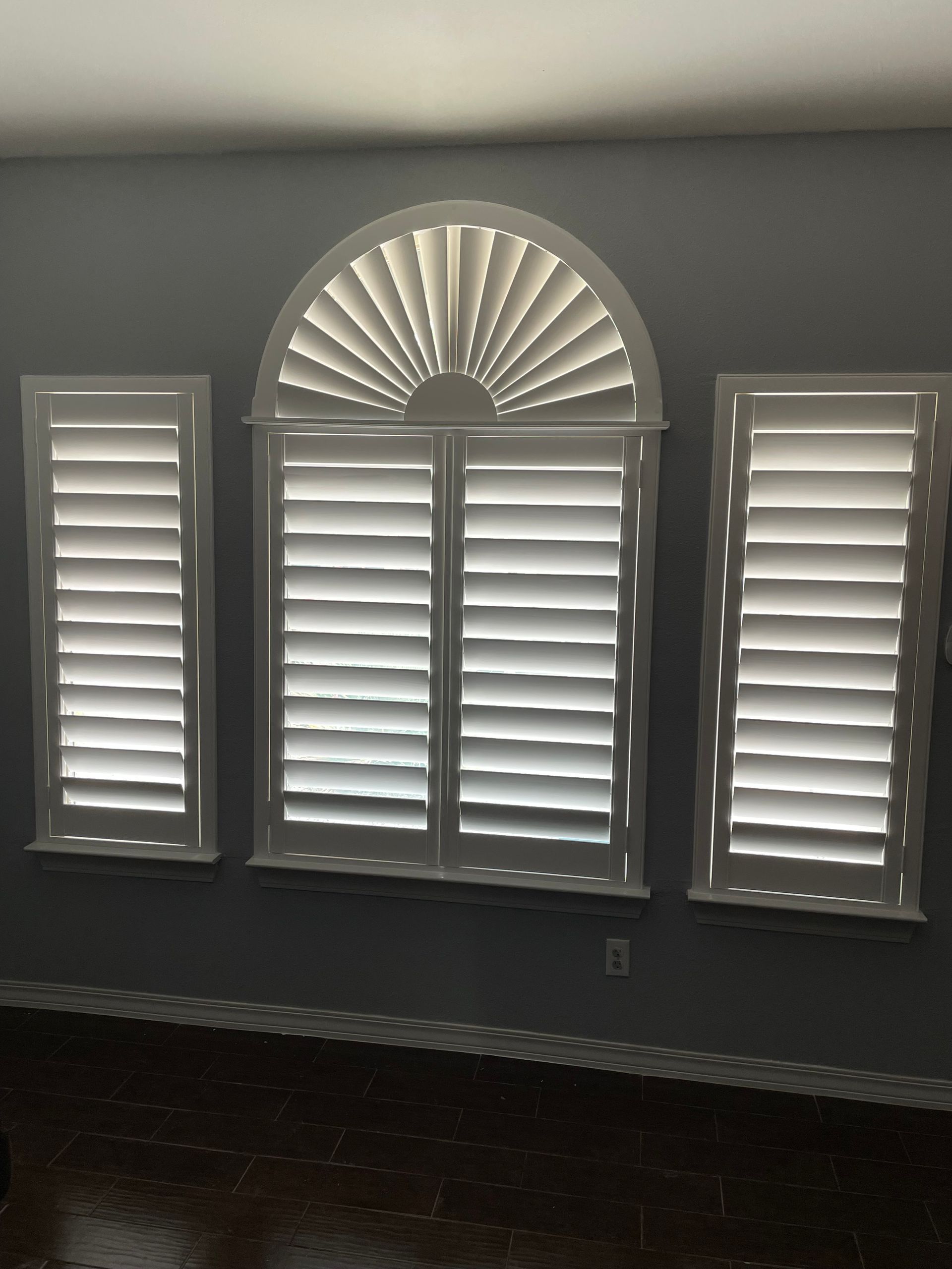 A room with a gray wall and white shutters on the windows
