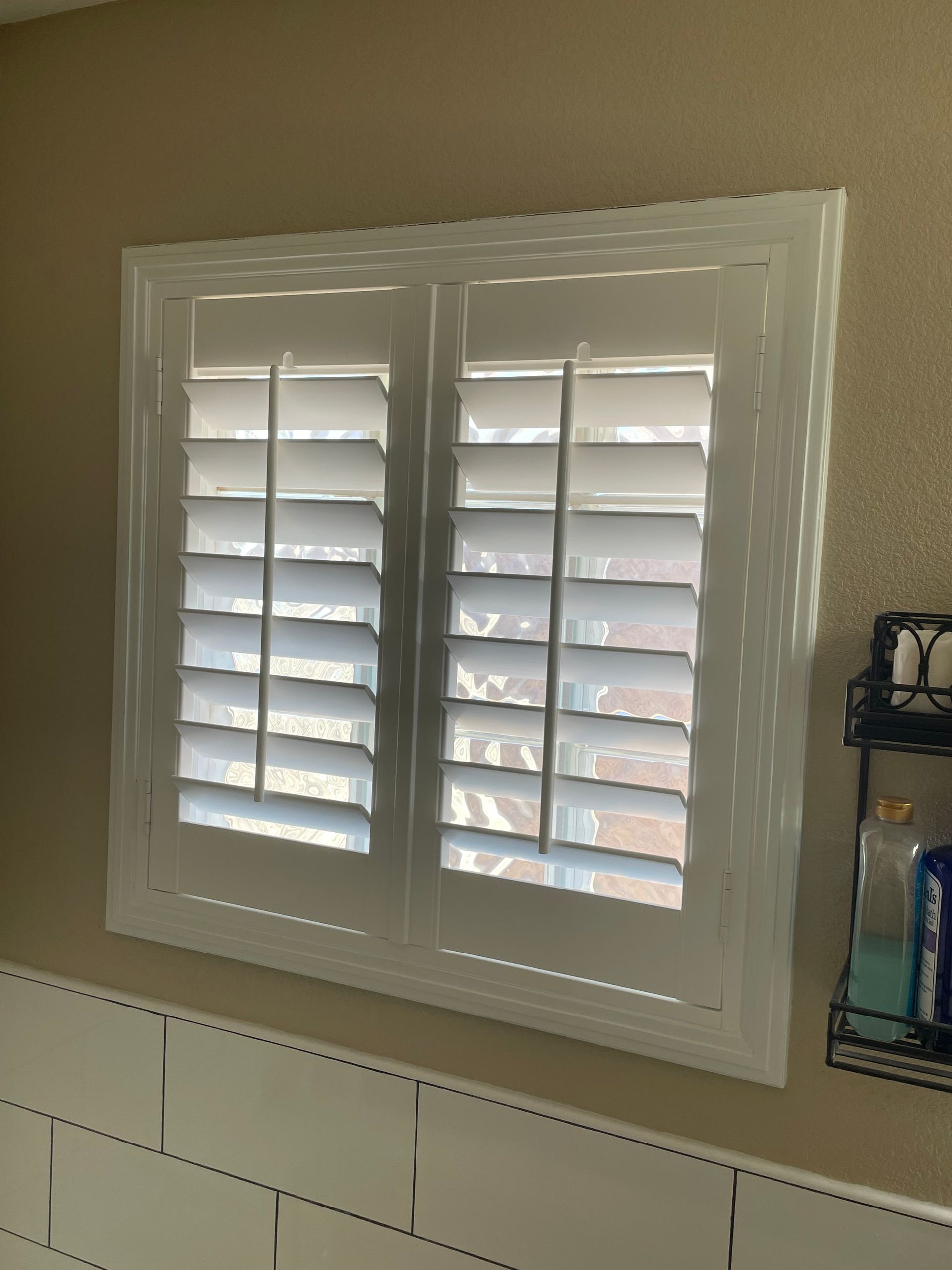 A bathroom window with white shutters on it