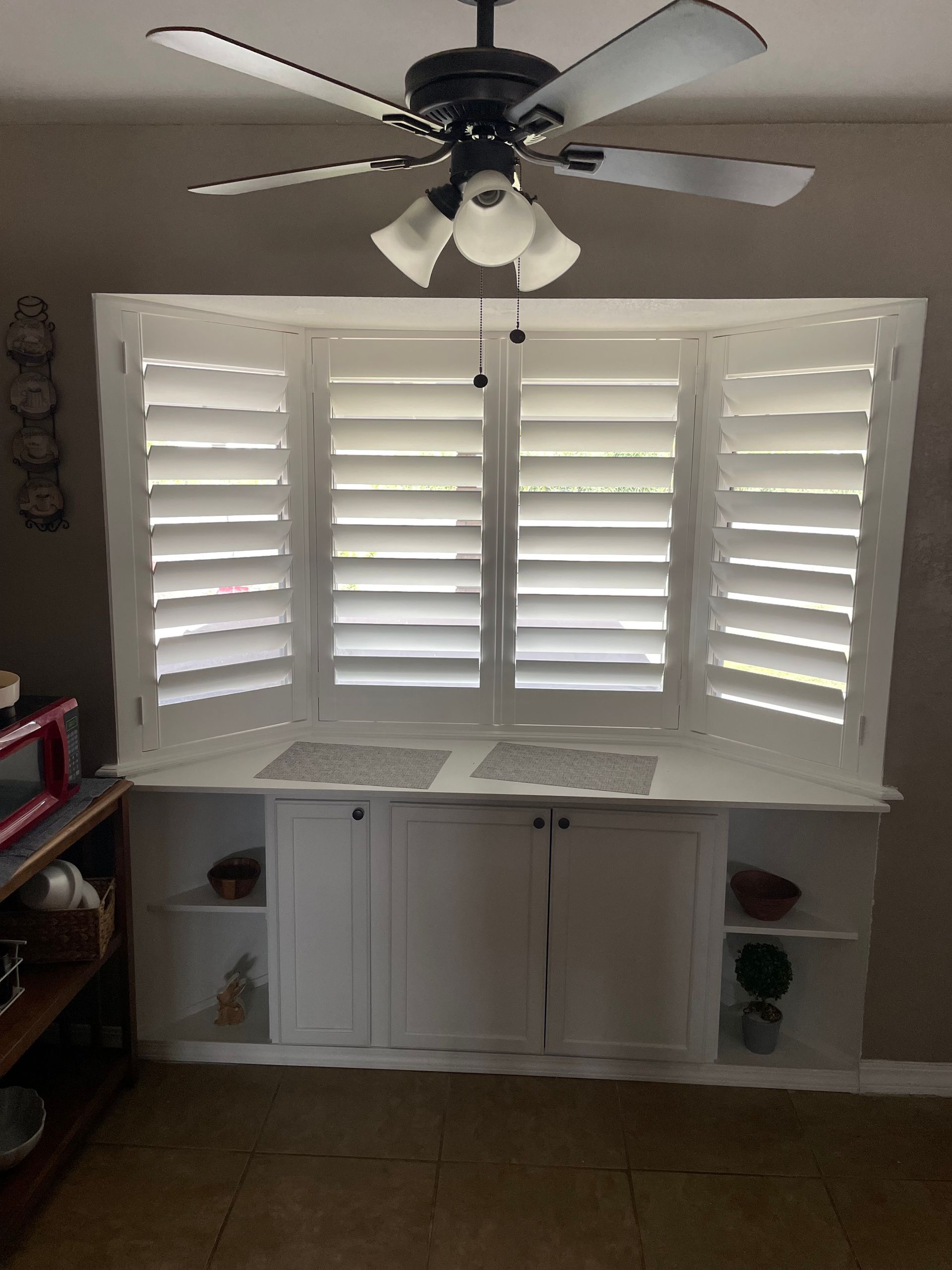 A ceiling fan is hanging from the ceiling above a window with white shutters.