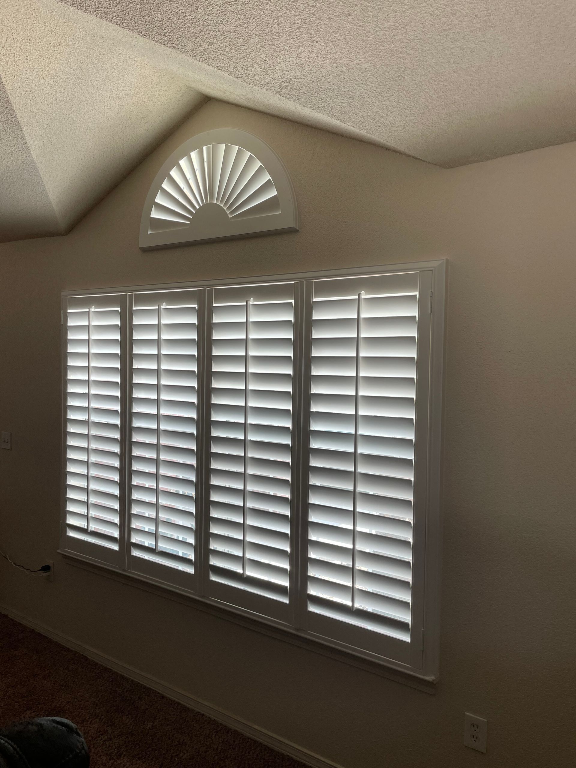 A room with white shutters on the windows and a fan on the ceiling.