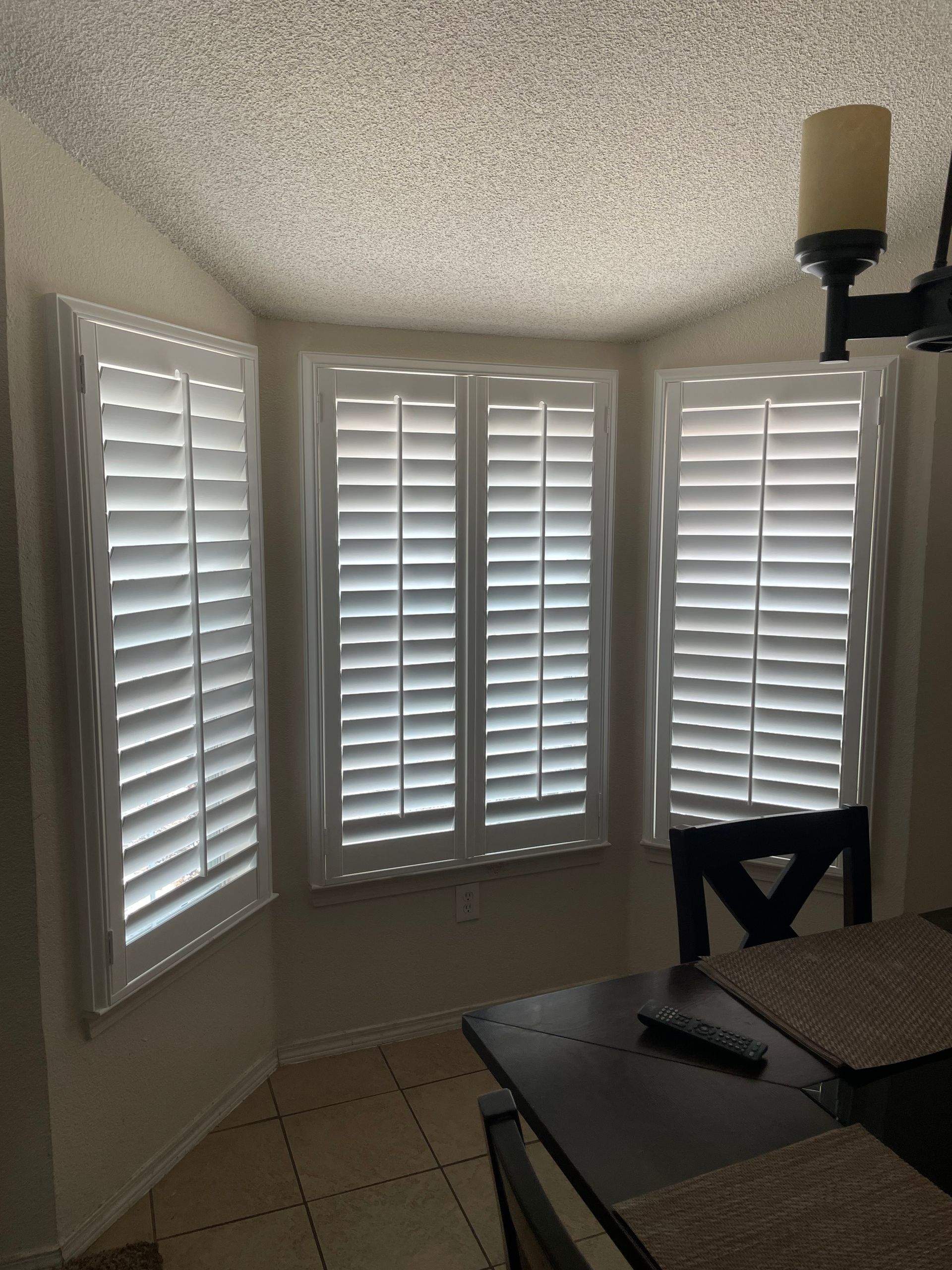 A dining room with a table and chairs and white shutters on the windows.