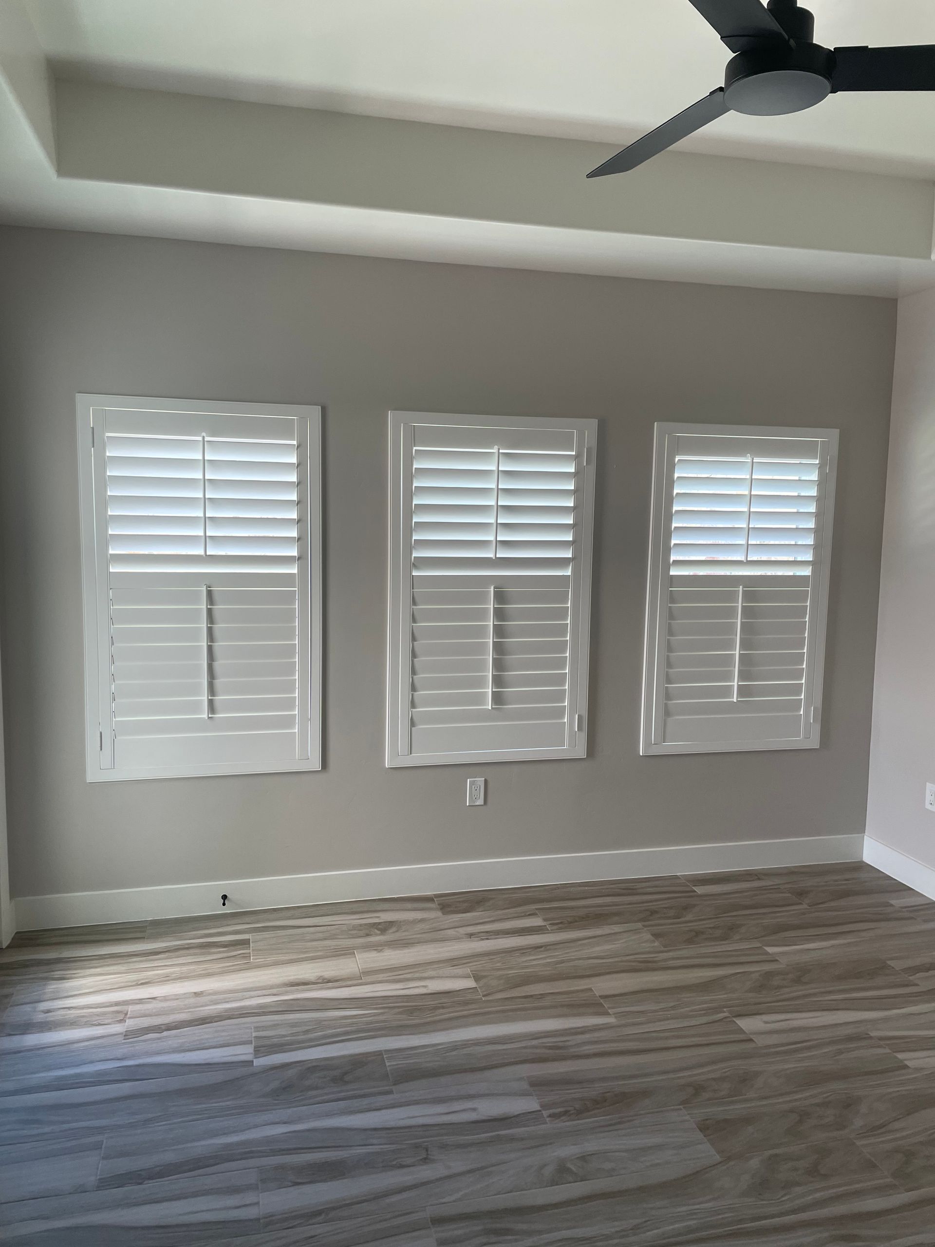 An empty room with three windows and a ceiling fan.