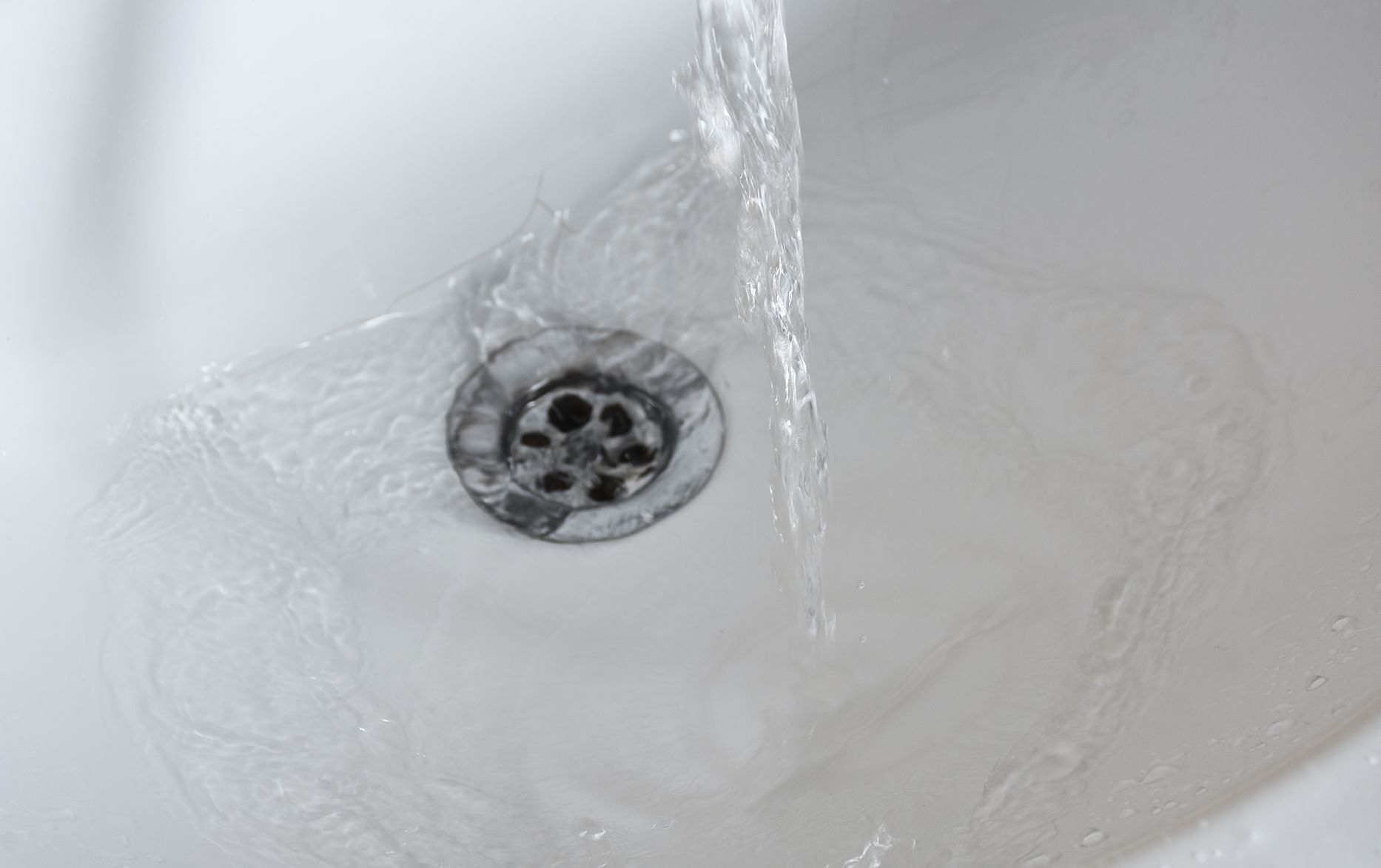 White porcelain sink with running water flowing into a metal drain.