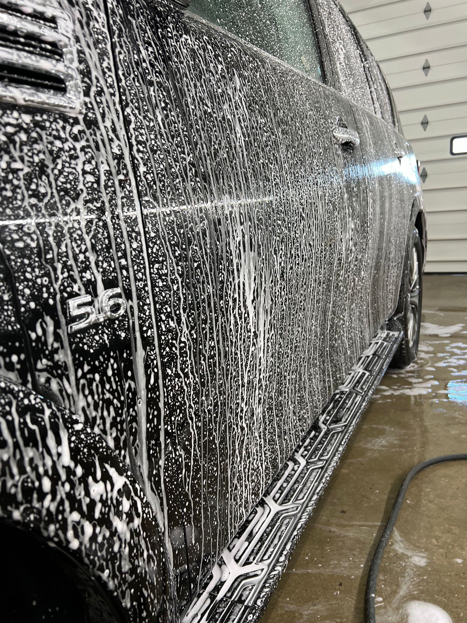 A car is covered in foam while being washed in a garage.