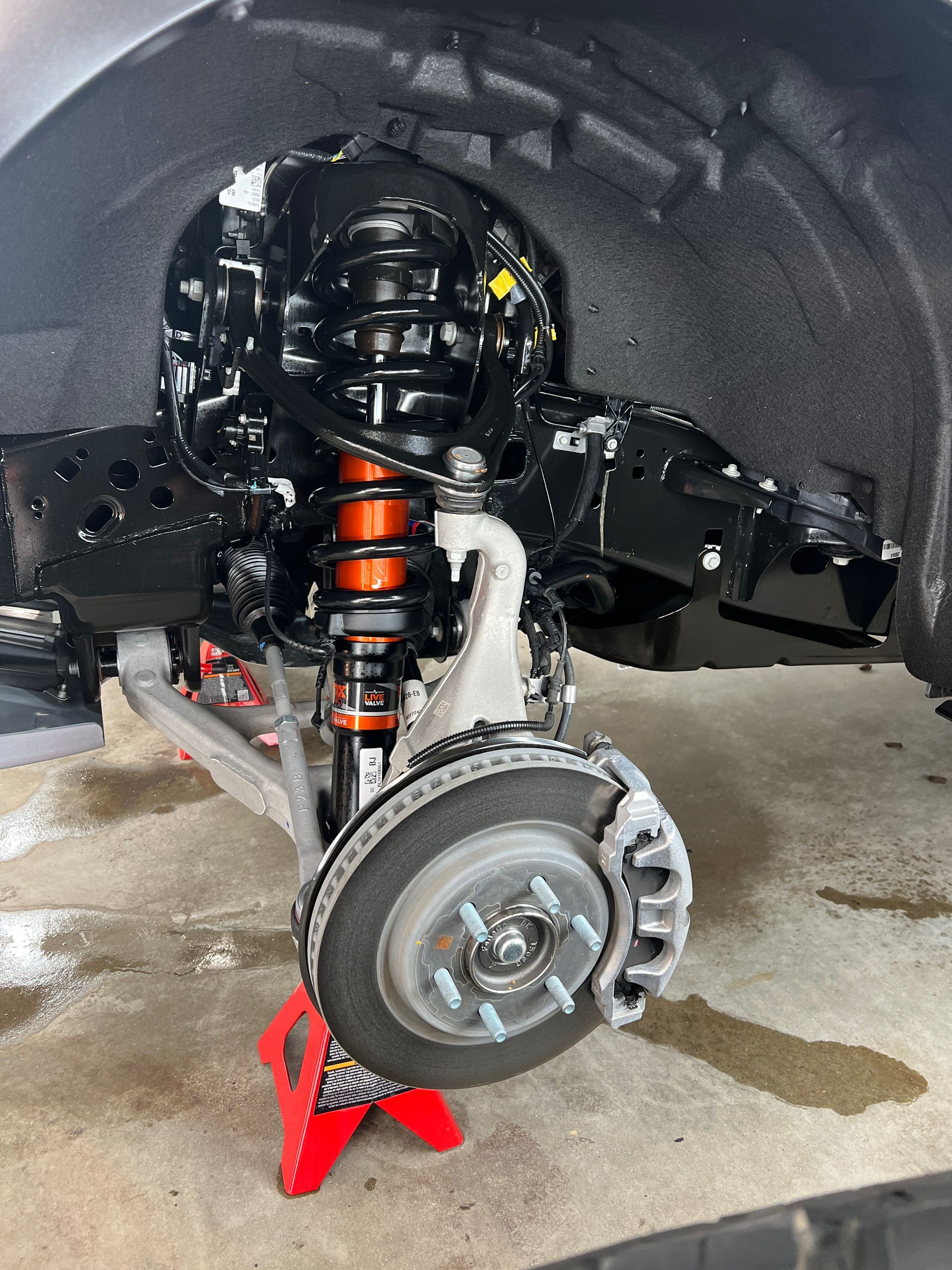 The front end of a car is sitting on a red jack stand.