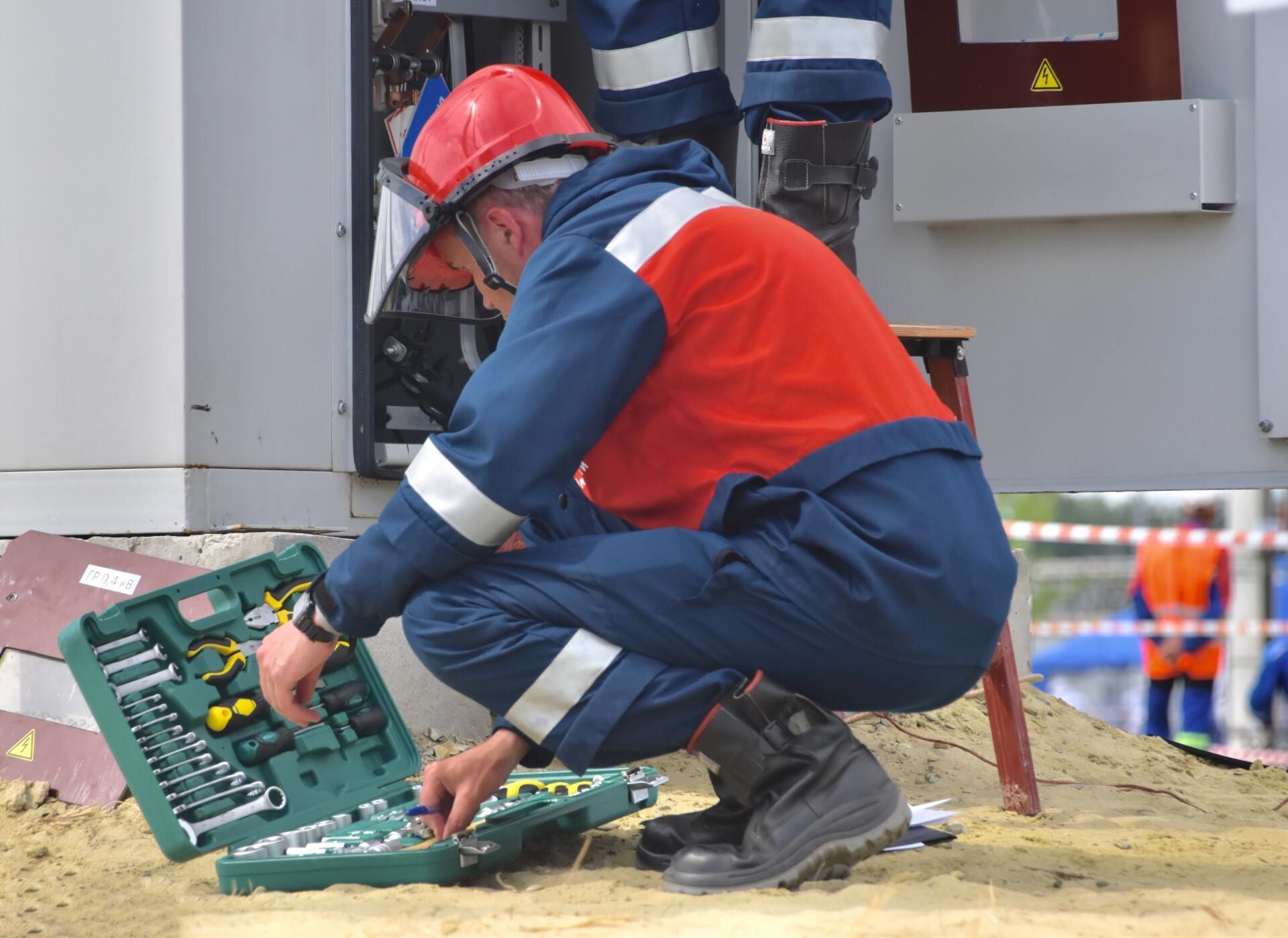 A man in a hard hat is kneeling down next to a box of tools.
