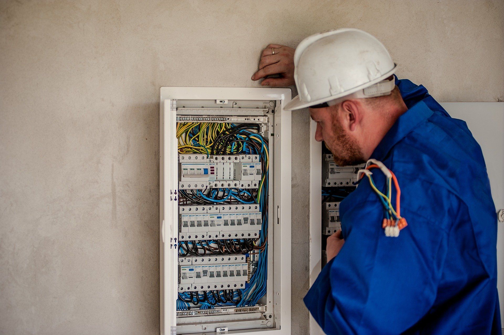 A man wearing a hard hat is working on an electrical box.