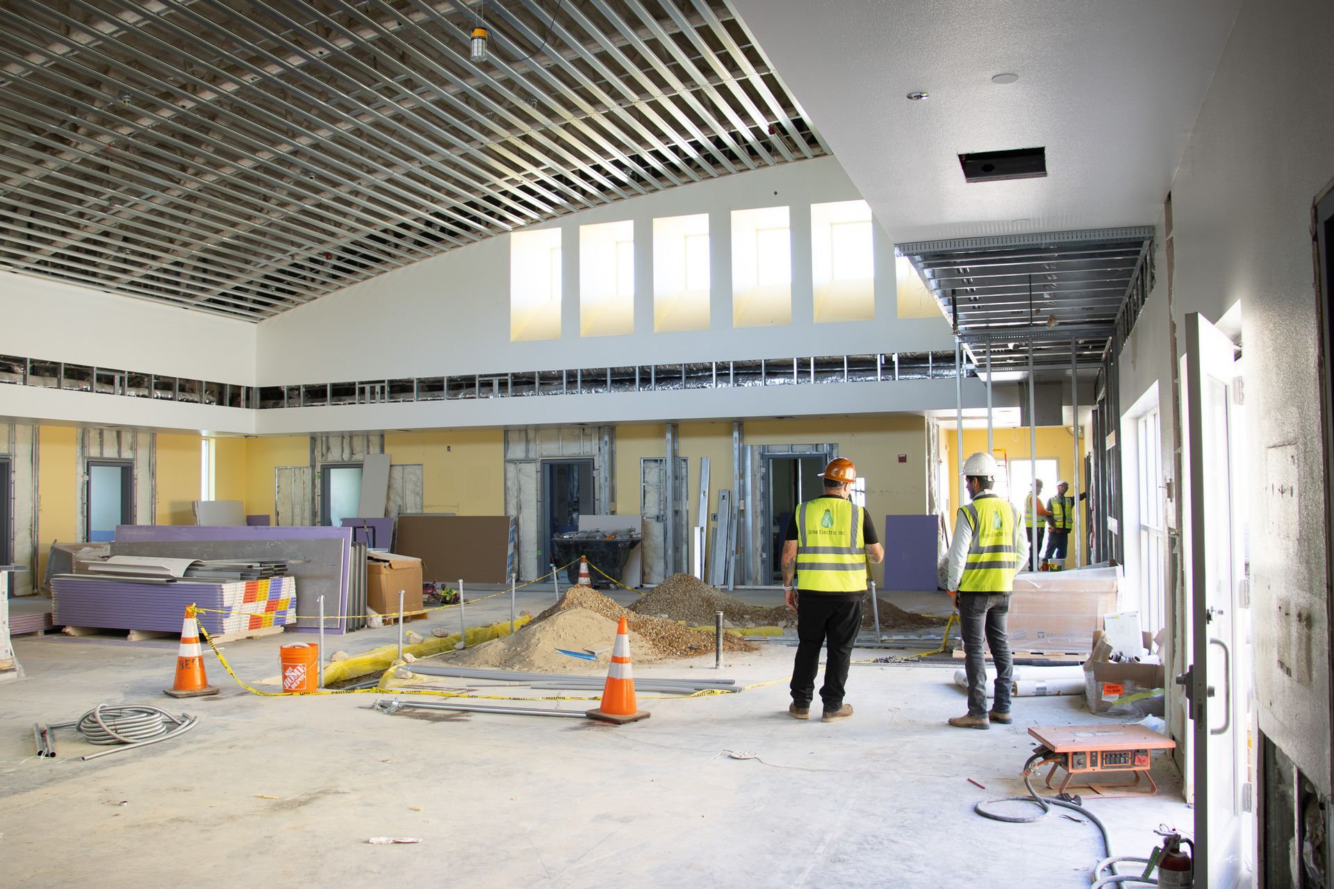 Construction workers in a bright room with scaffolding, tools, and debris during interior renovation.
