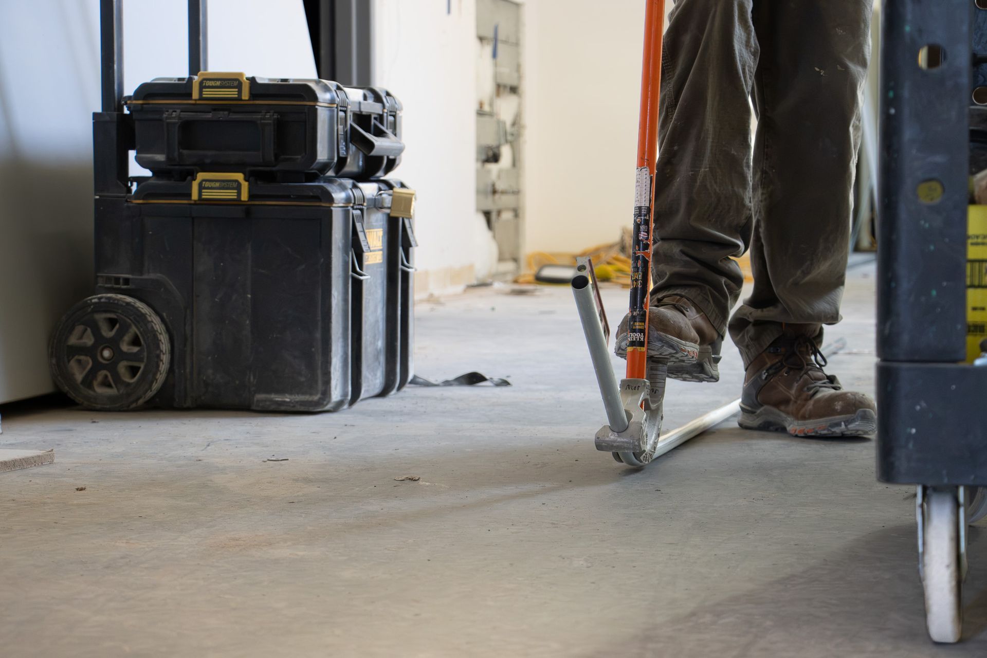 Construction worker’s legs with a jackhammer on a concrete floor, beside stacked tool cases.
