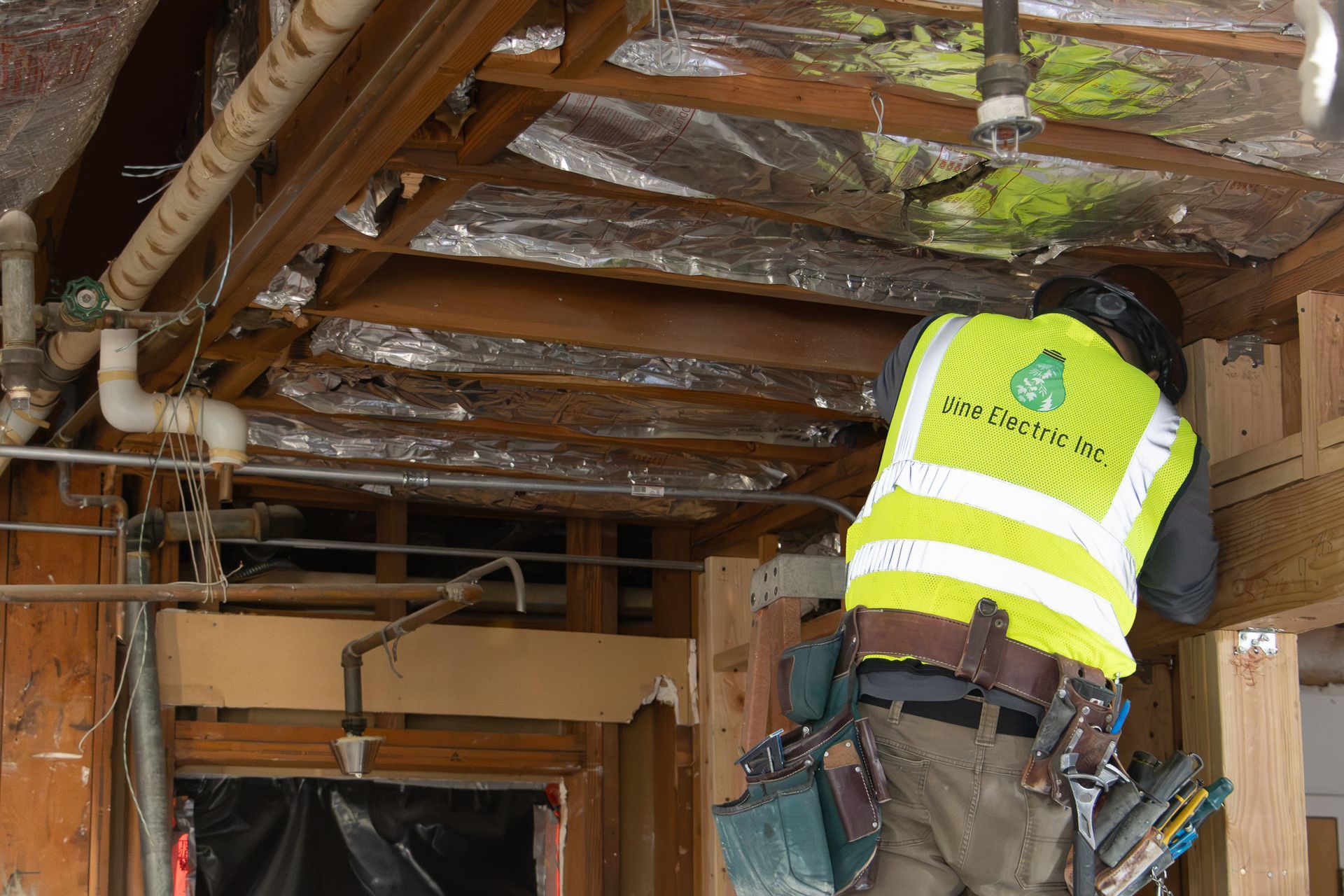 Worker in a neon safety vest inspecting exposed ceiling wiring and insulation in a building interior