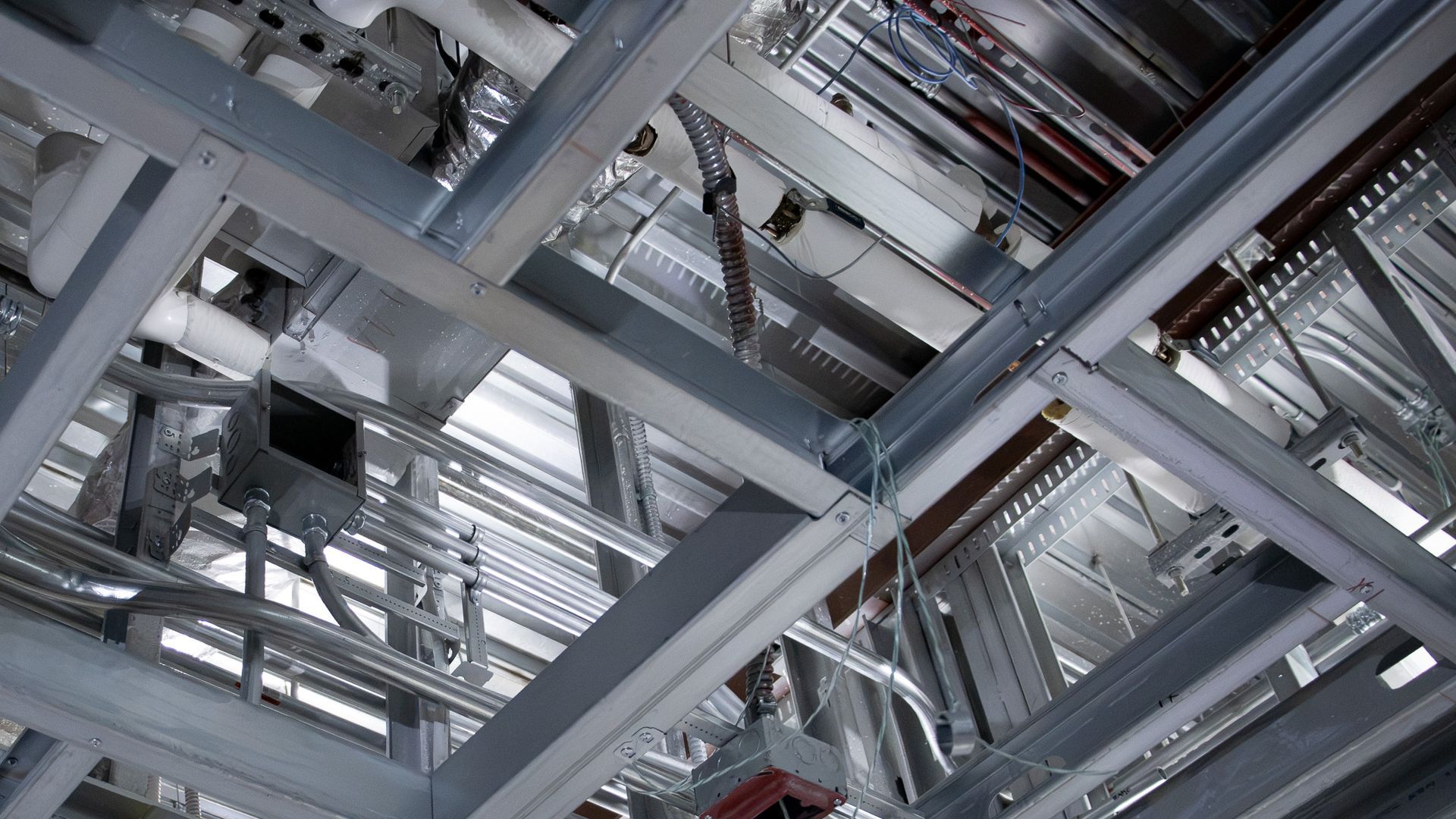 Steel beams and pipes crisscross the ceiling of an industrial interior.