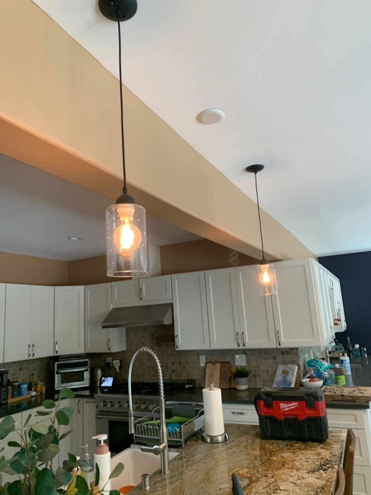 Kitchen with white cabinets, pendant lights, and a granite island counter with plants and small appliances.