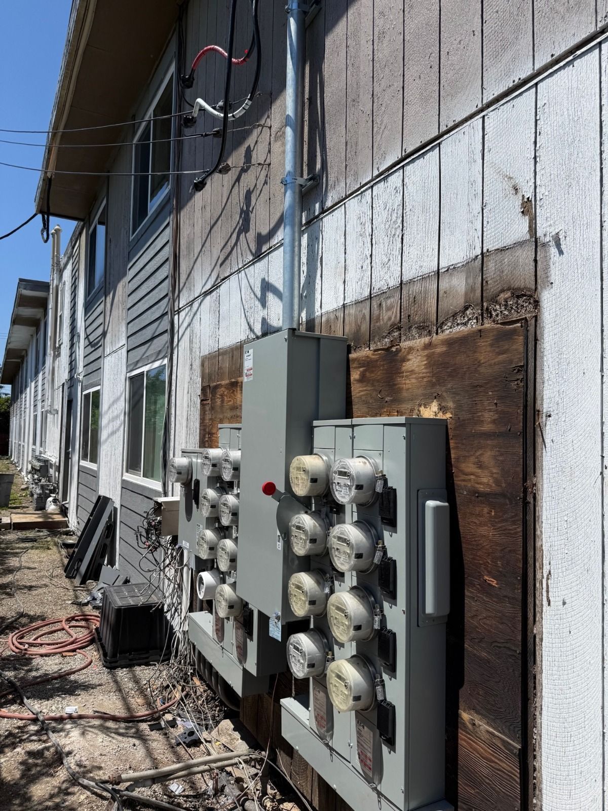 Row of utility meters and electrical boxes mounted on a weathered building exterior with overhead wires