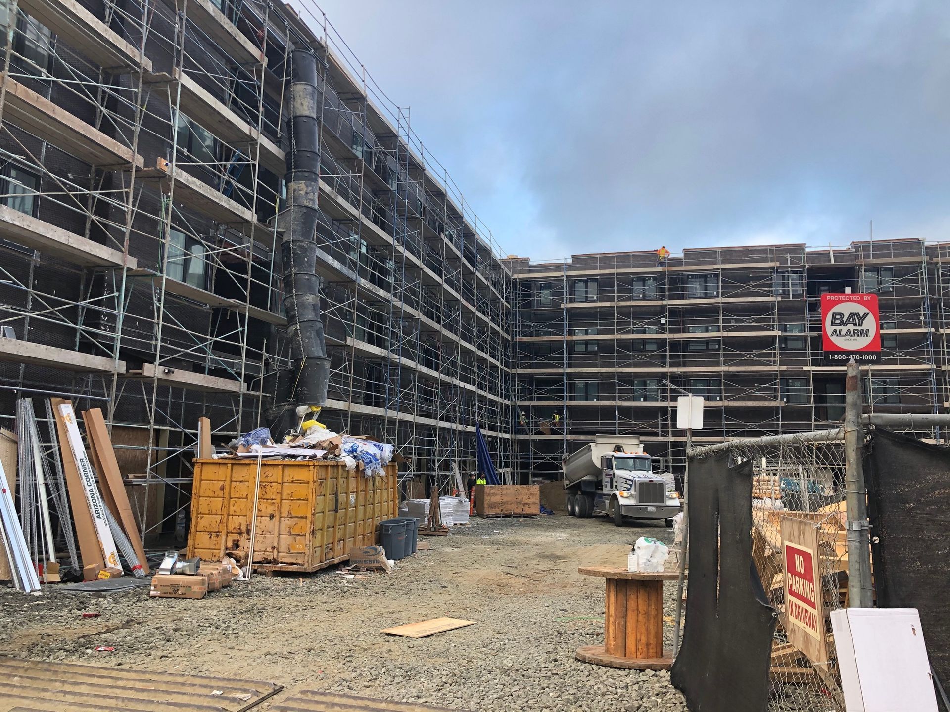 Scaffolding-covered apartment buildings under construction with materials and a truck in the yard
