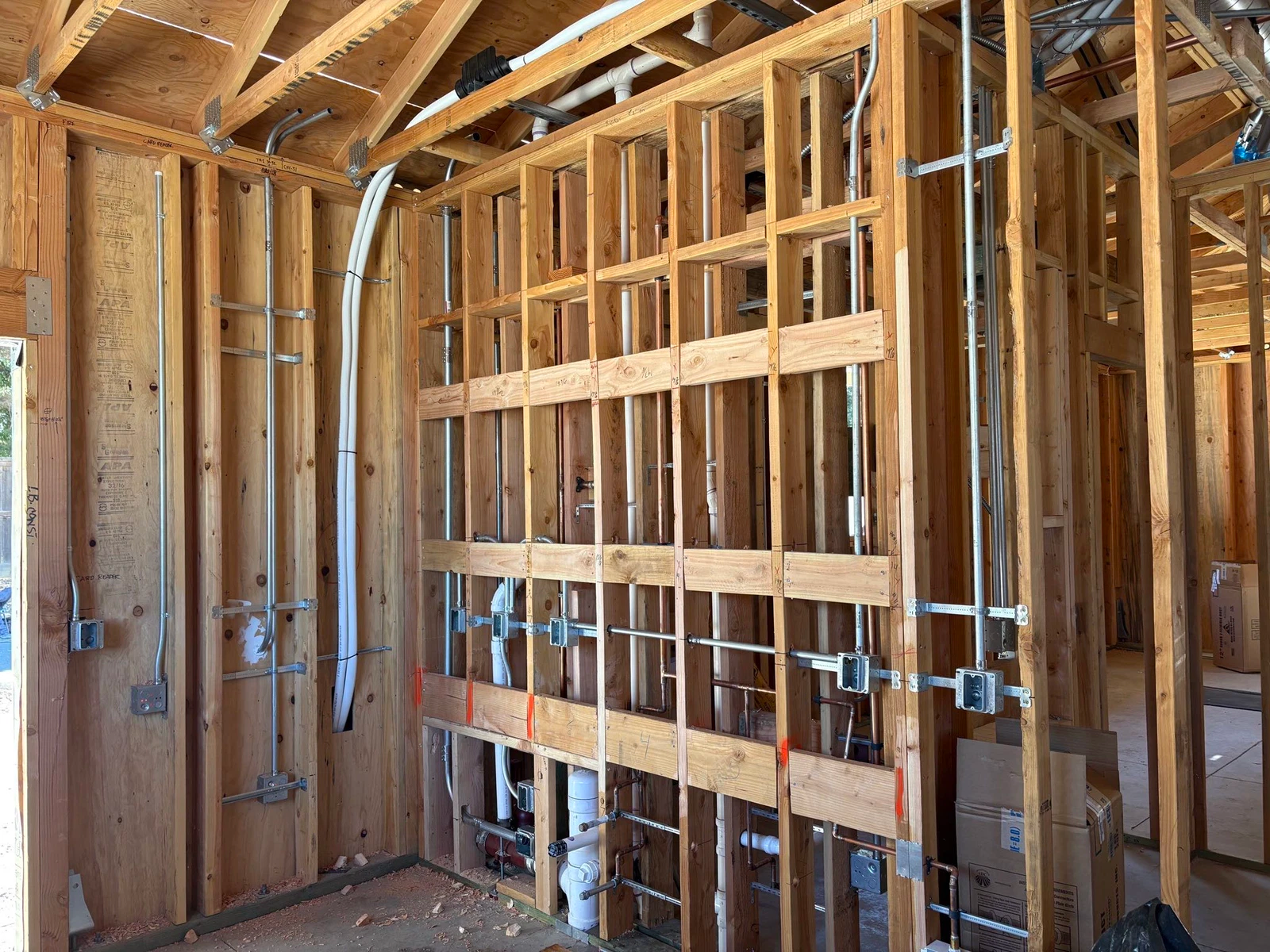Interior view of a building under construction, showing wooden framing, electrical wiring, and plumbing.