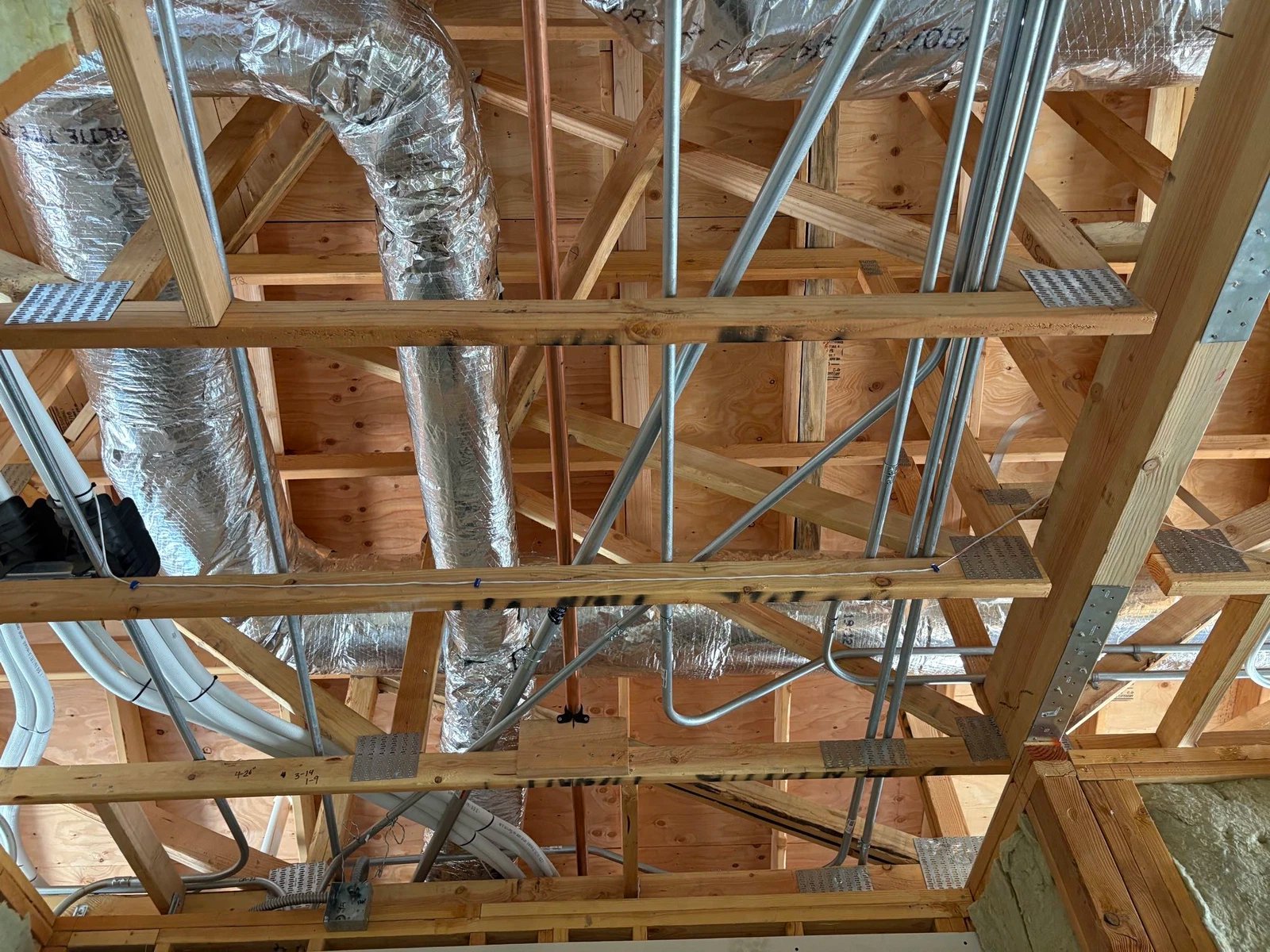 Wooden roof trusses with ductwork, electrical conduit, and insulation visible.