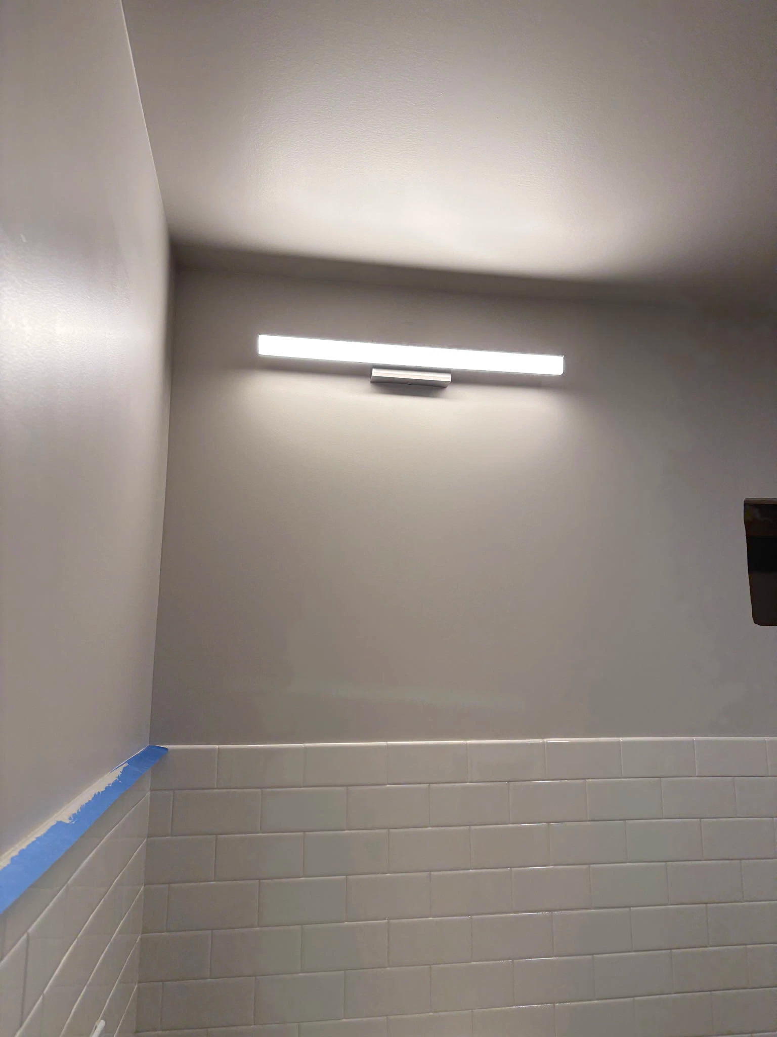 A modern bathroom with a rectangular light fixture above white subway tiles. Gray walls.