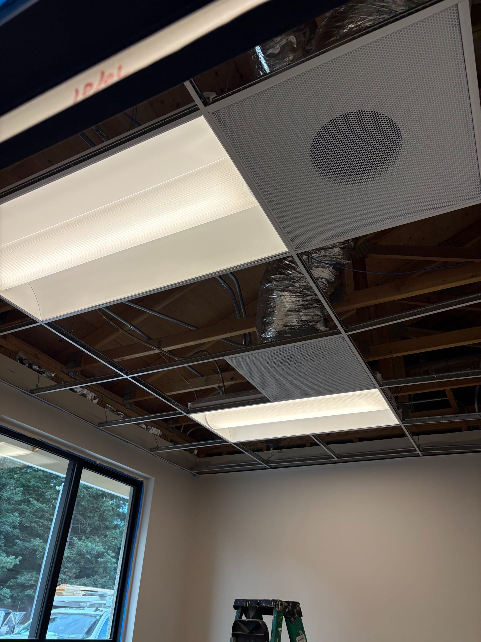 Ceiling panels with lights and decorative metalwork installed in a room. A ladder is present.