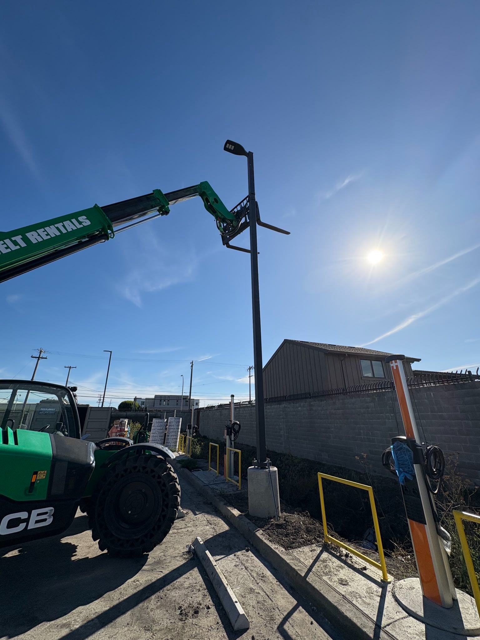 Green construction lift truck beside a brick building under a bright blue sky