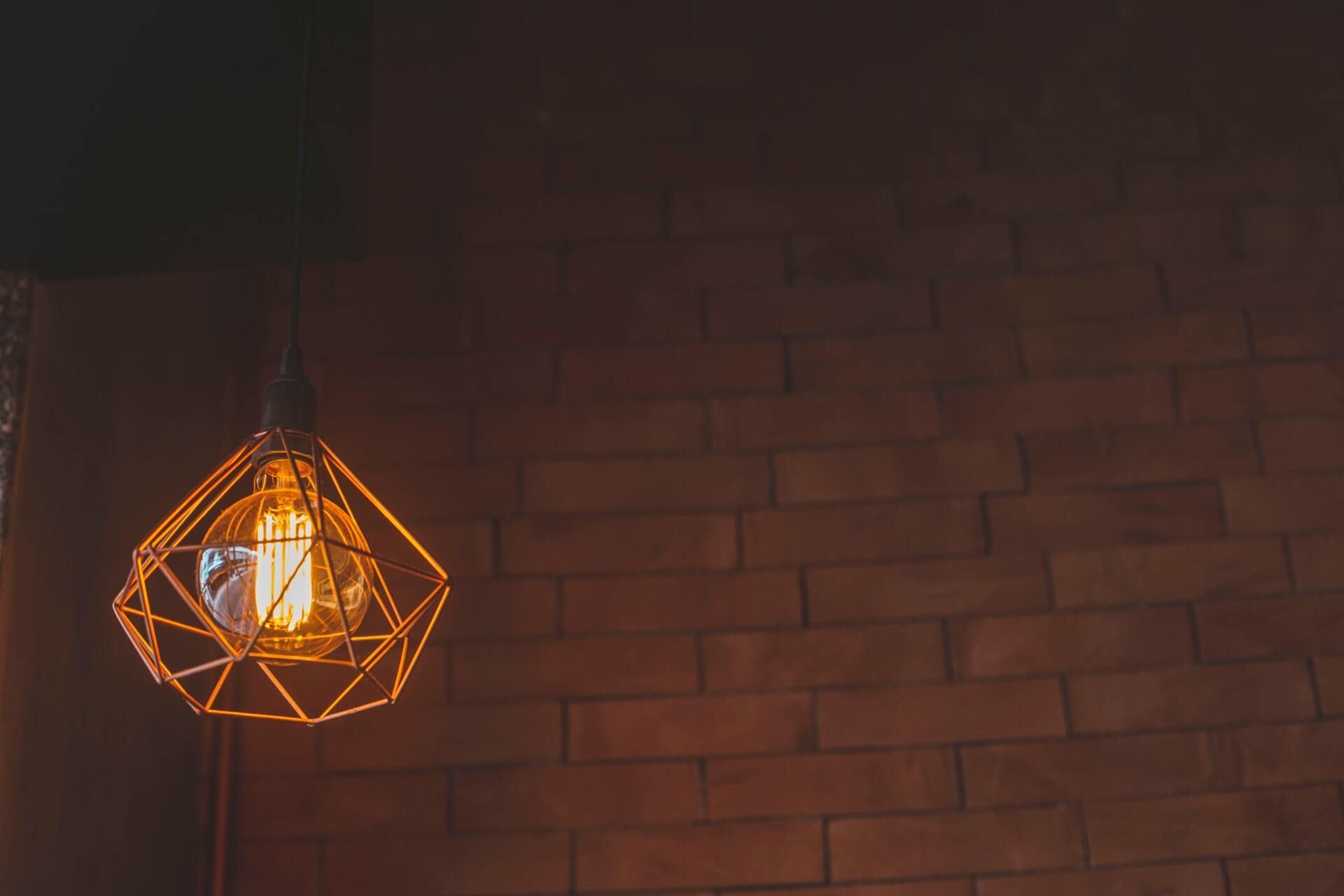 A pendant light is hanging from the ceiling in front of a brick wall.