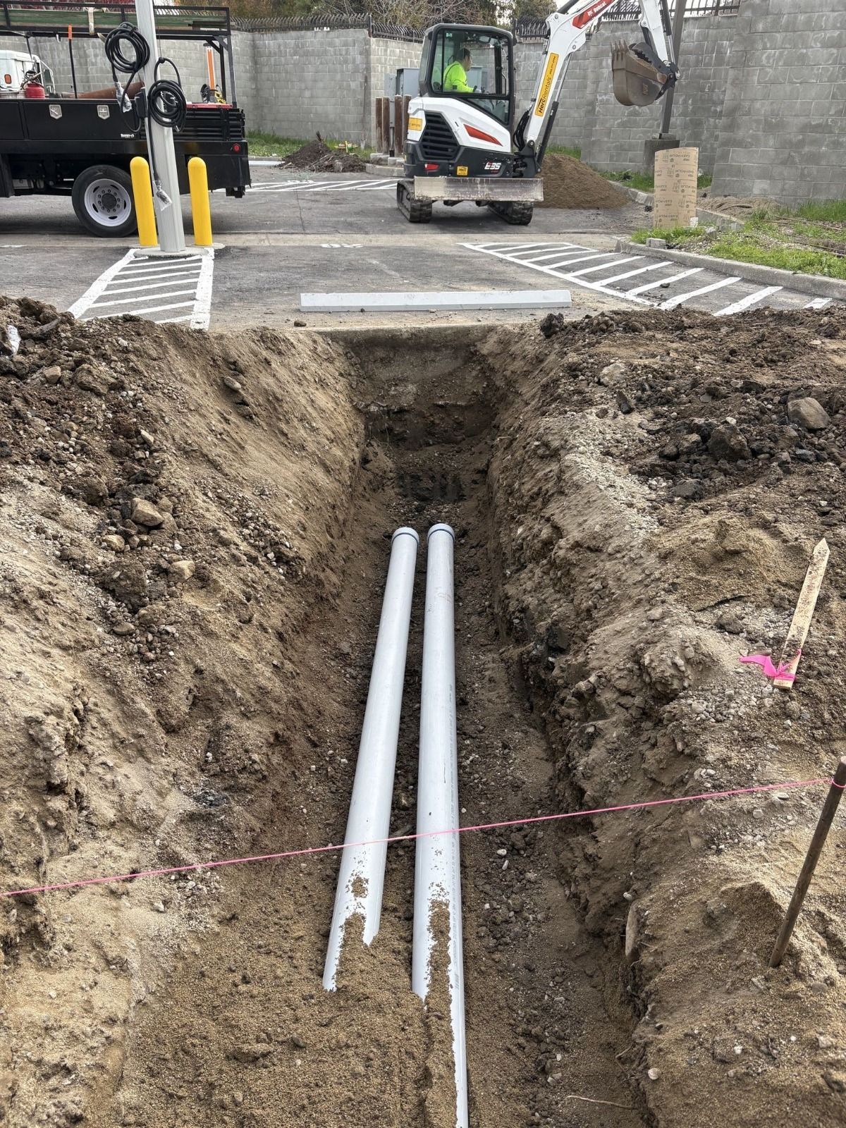Open road trench with exposed white utility pipes beneath a construction site.