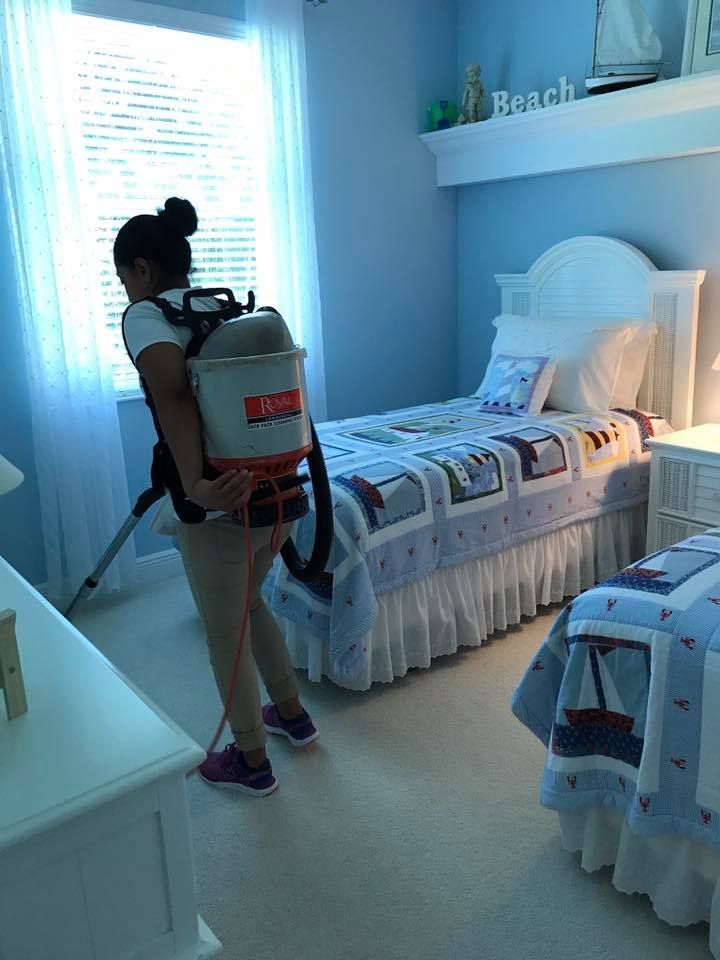 A woman is cleaning a bedroom with a vacuum cleaner.