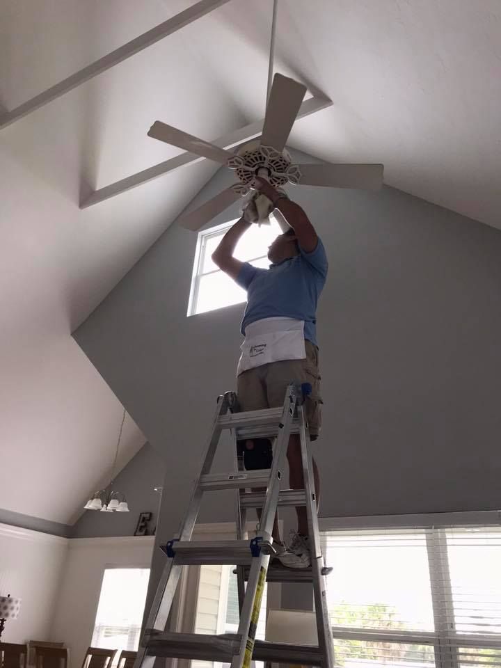 A man is standing on a ladder fixing a ceiling fan.