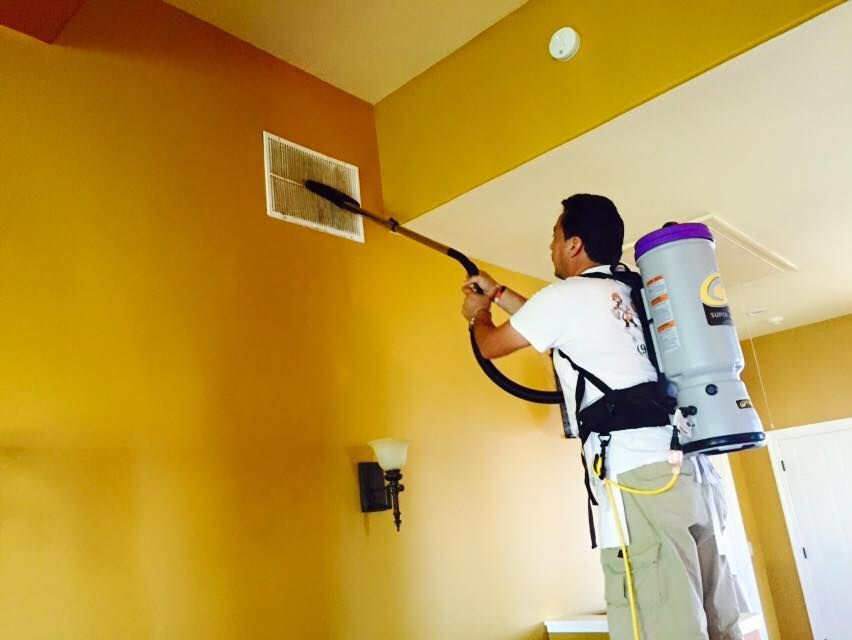 A man is cleaning a vent with a backpack vacuum cleaner.