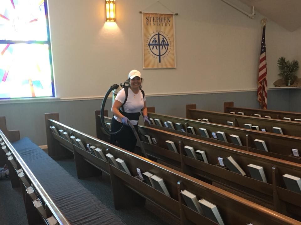 A woman is cleaning the aisles of a church with a vacuum cleaner.