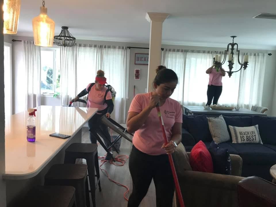 A woman in a pink shirt is mopping the floor in a living room.