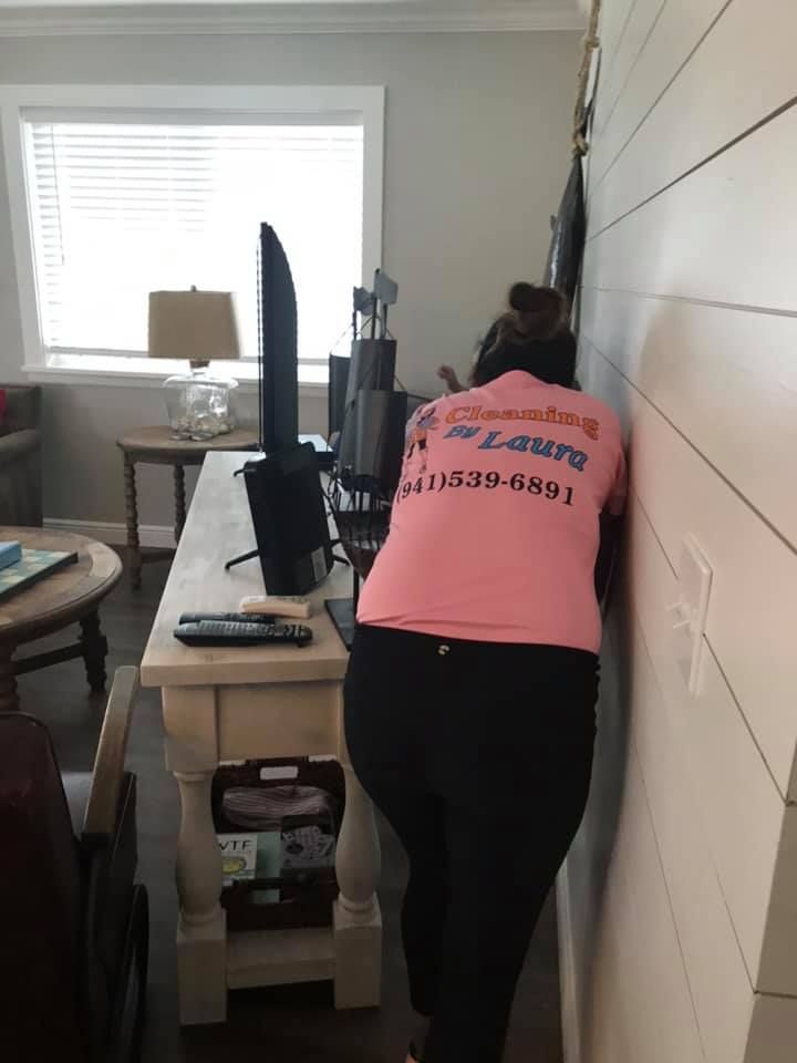 A woman in a pink shirt is leaning against a wall in a living room.
