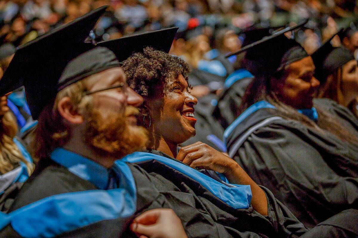 Graduates in caps and gowns seated in an auditorium, smiling during a ceremony