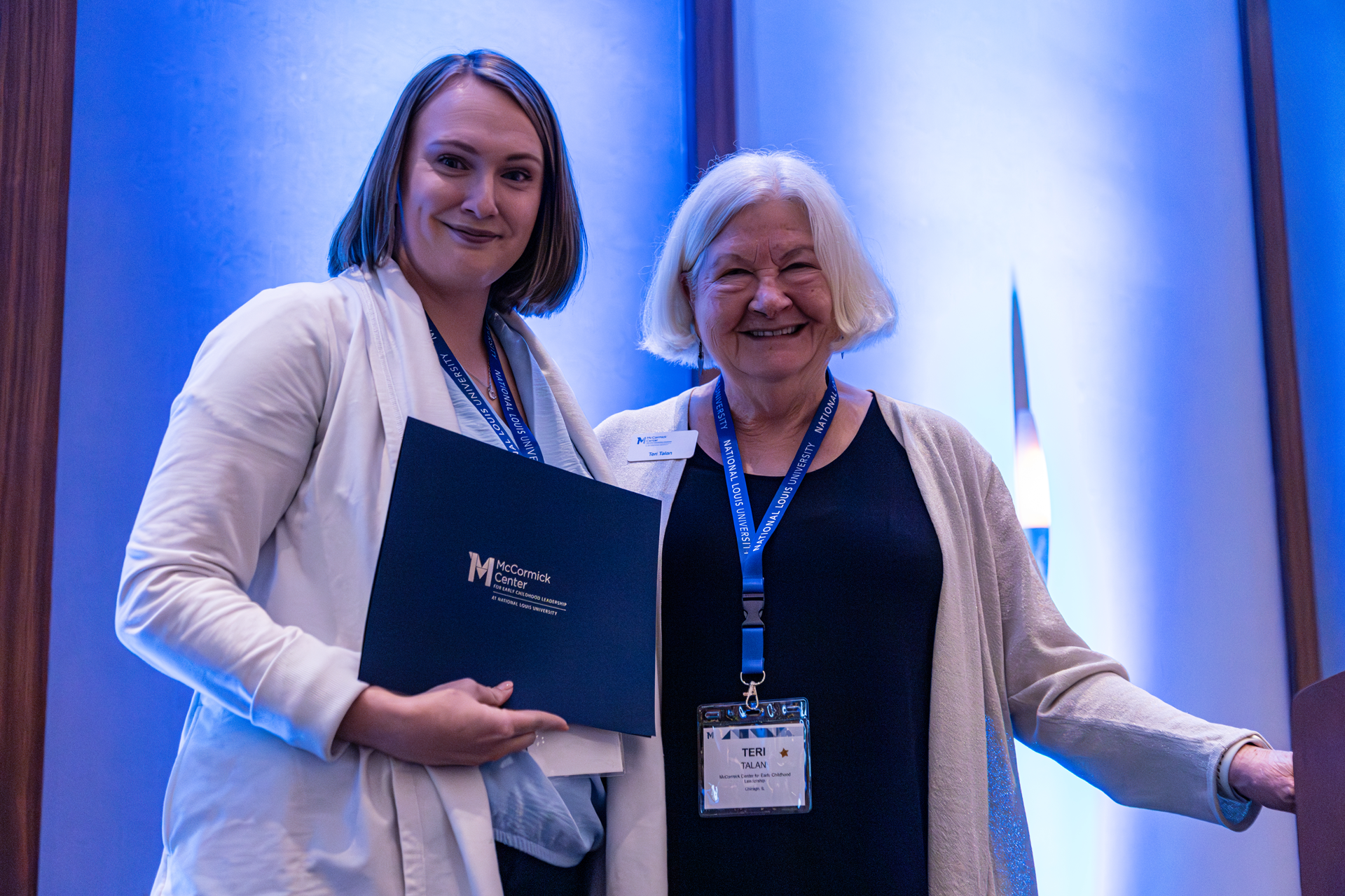 Woman presents award to another woman on a stage; both smiling.