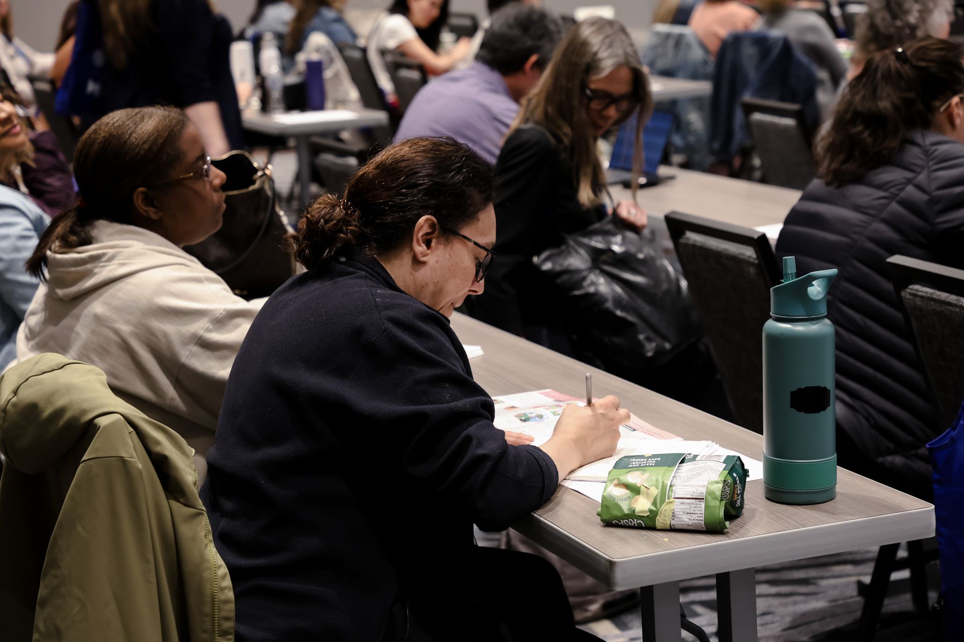 A woman is sitting at a table writing on a piece of paper.
