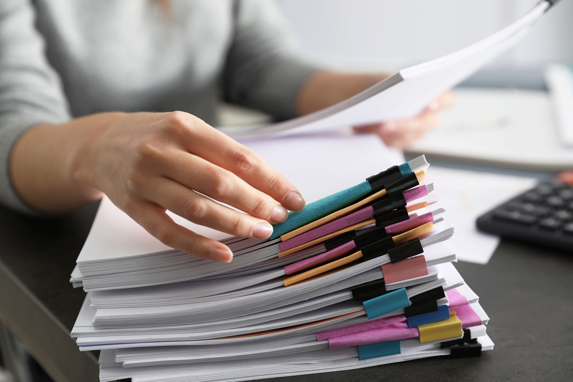 Person sorts through a stack of papers, organized with colorful binder clips.