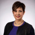 A woman wearing a purple shirt and a black jacket is smiling for the camera.