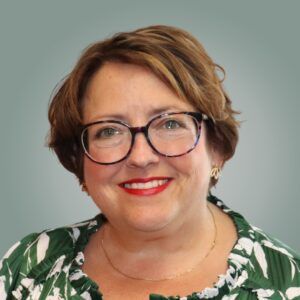 A woman wearing glasses and a green shirt is smiling.