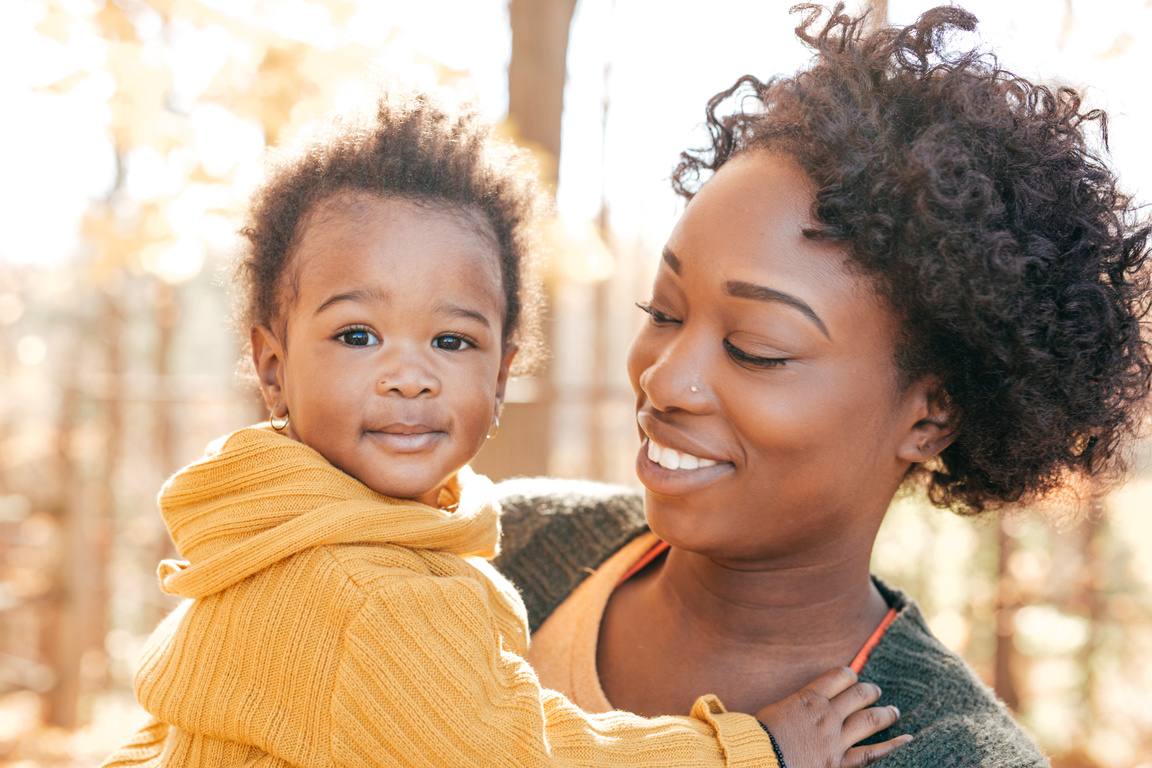 Woman smiling at a child in a yellow sweater outdoors in warm sunlight