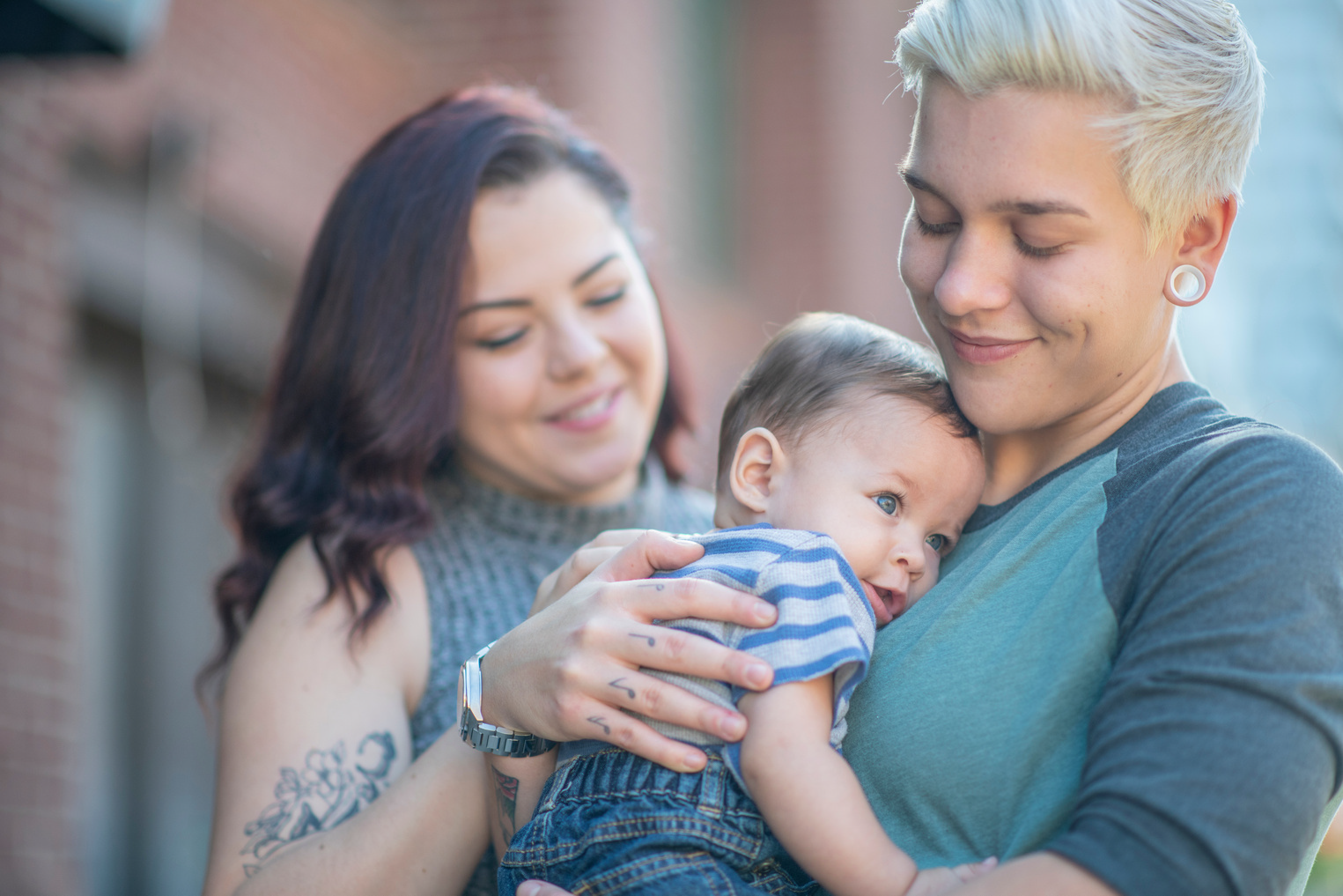 Three people smiling while holding a sleeping baby outdoors